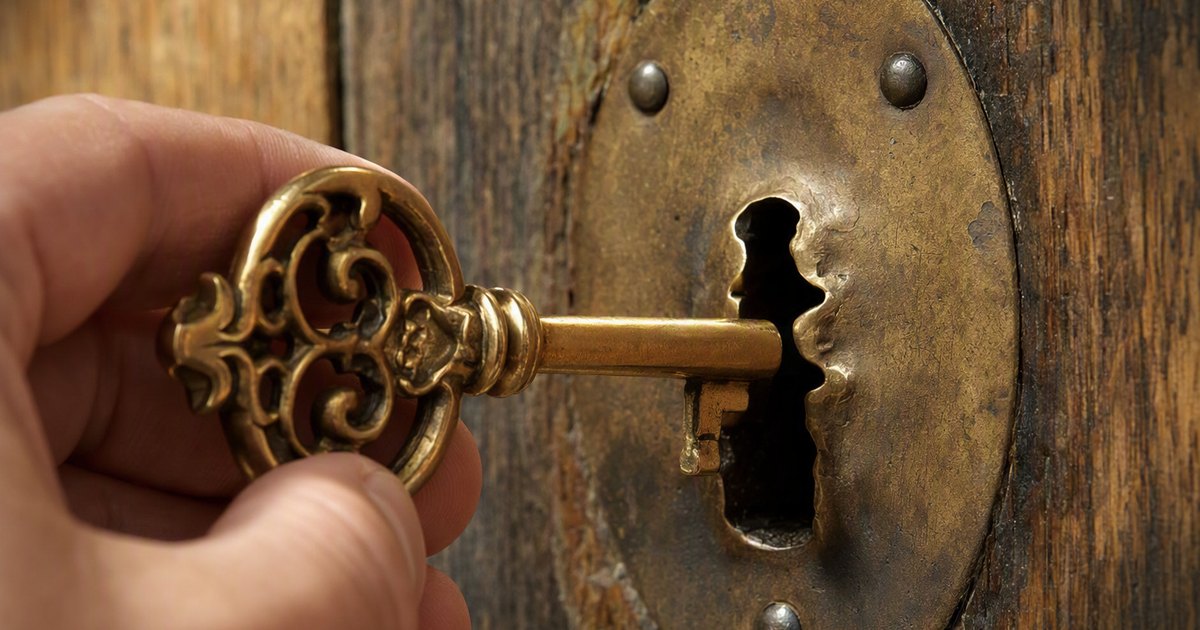 A hand holds a golden key to an old brass door lock. The keyhole is visibly warped into a different shape